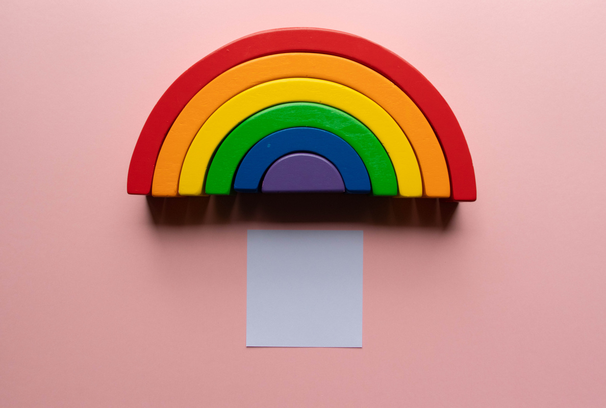 Bright wooden rainbow toy on a pink background with a blank white box for text- creative flat lay composition